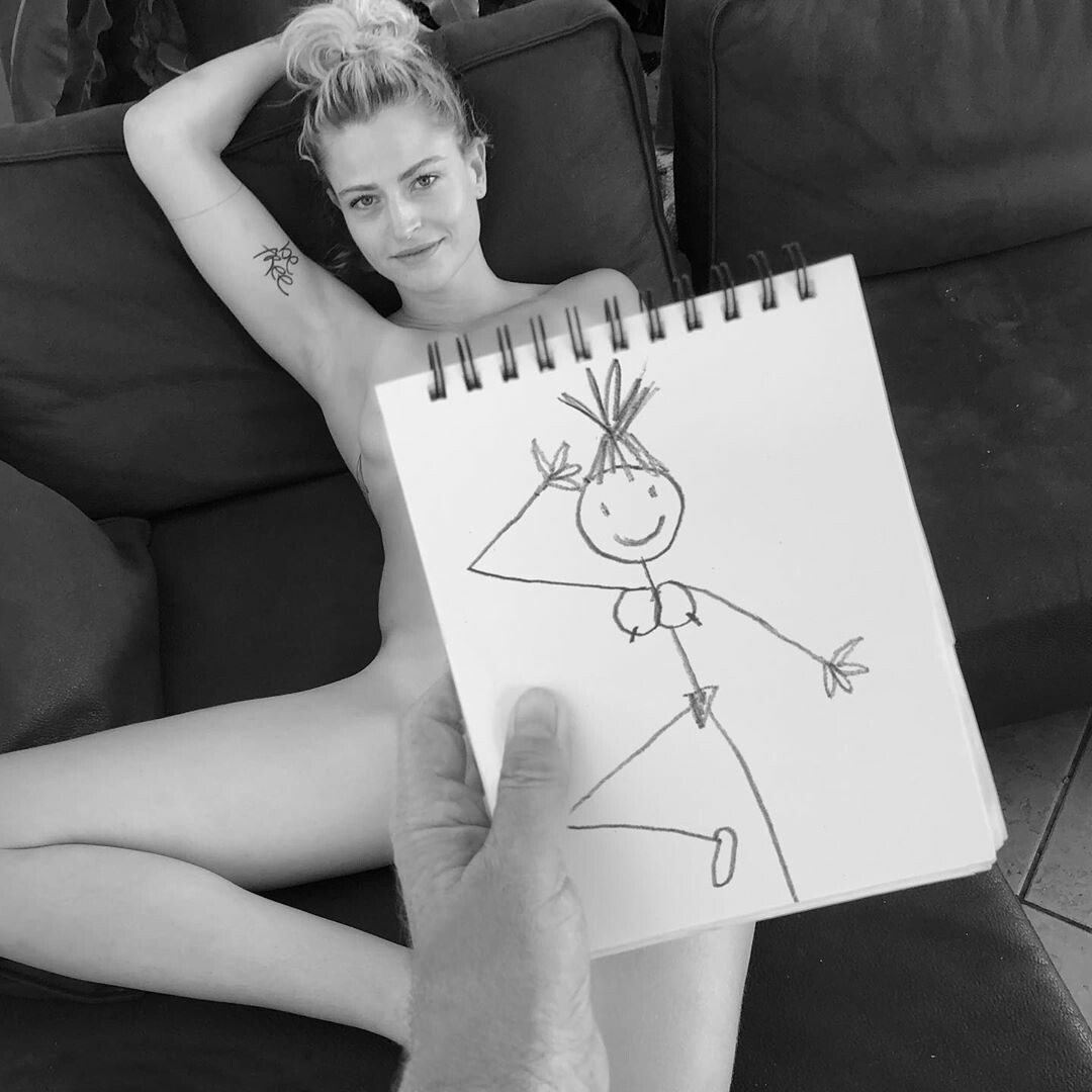 Black and white photo of a young woman lying on a sofa posing for a drawing and a man's hand holding a notepad above her with a very crude schematic drawing of a female body